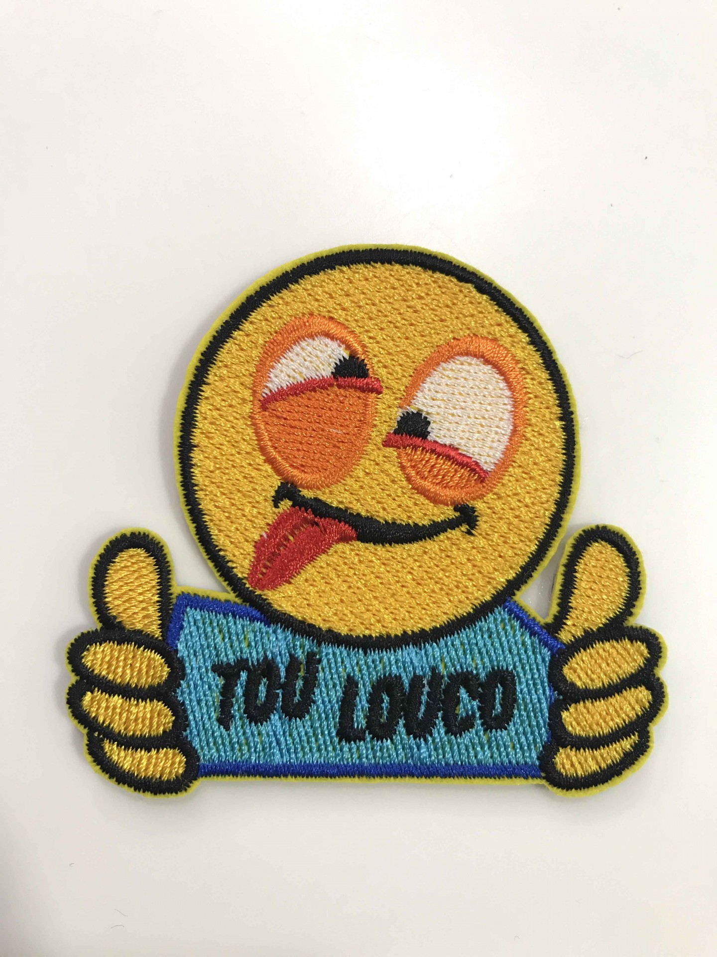 Emblema bordado emoji amarelo com língua de fora e sinal de polegar para cima com texto YOU LOUCO