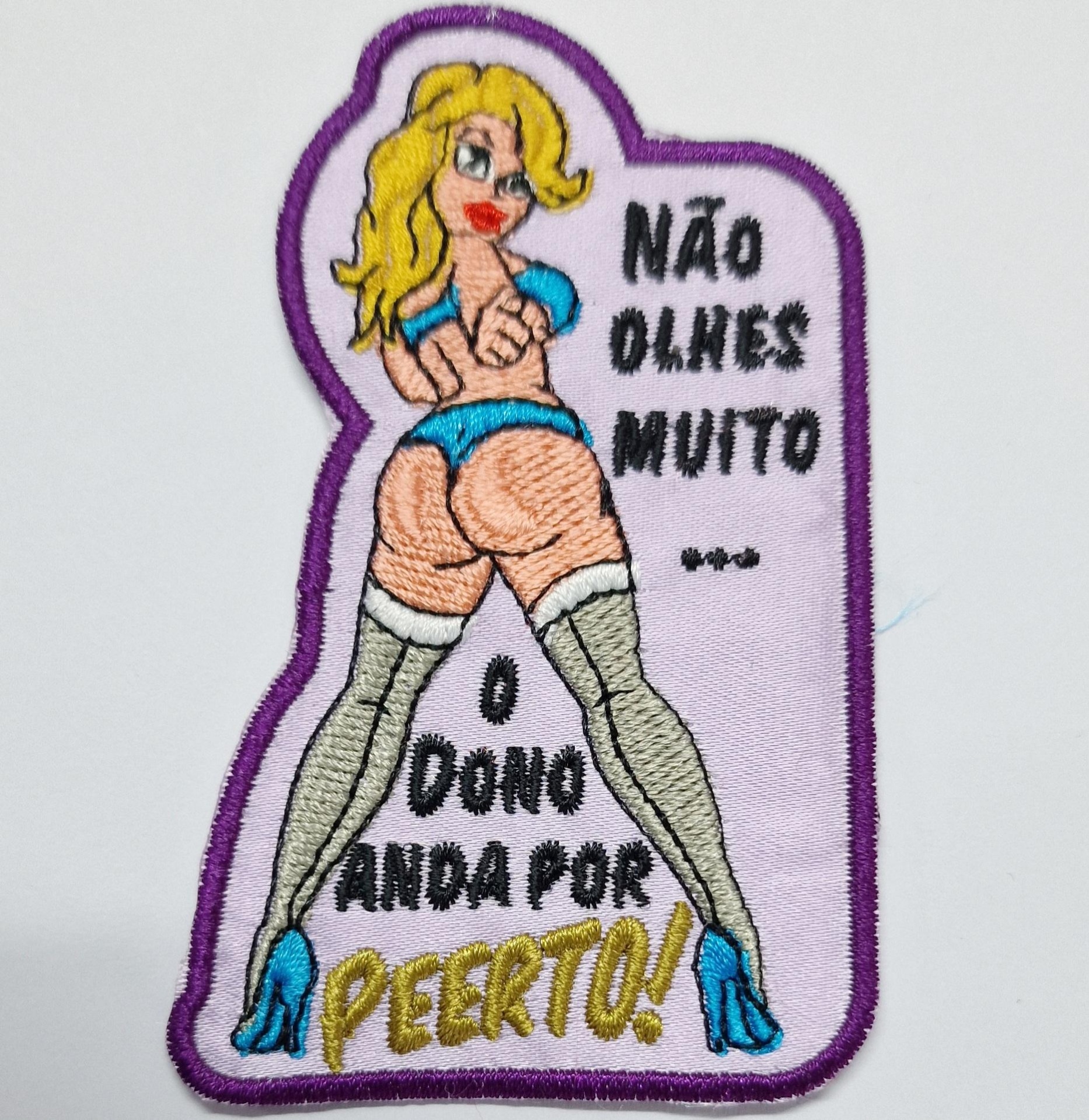 Emblema bordado com mulher loira em lingerie azul e texto em português.