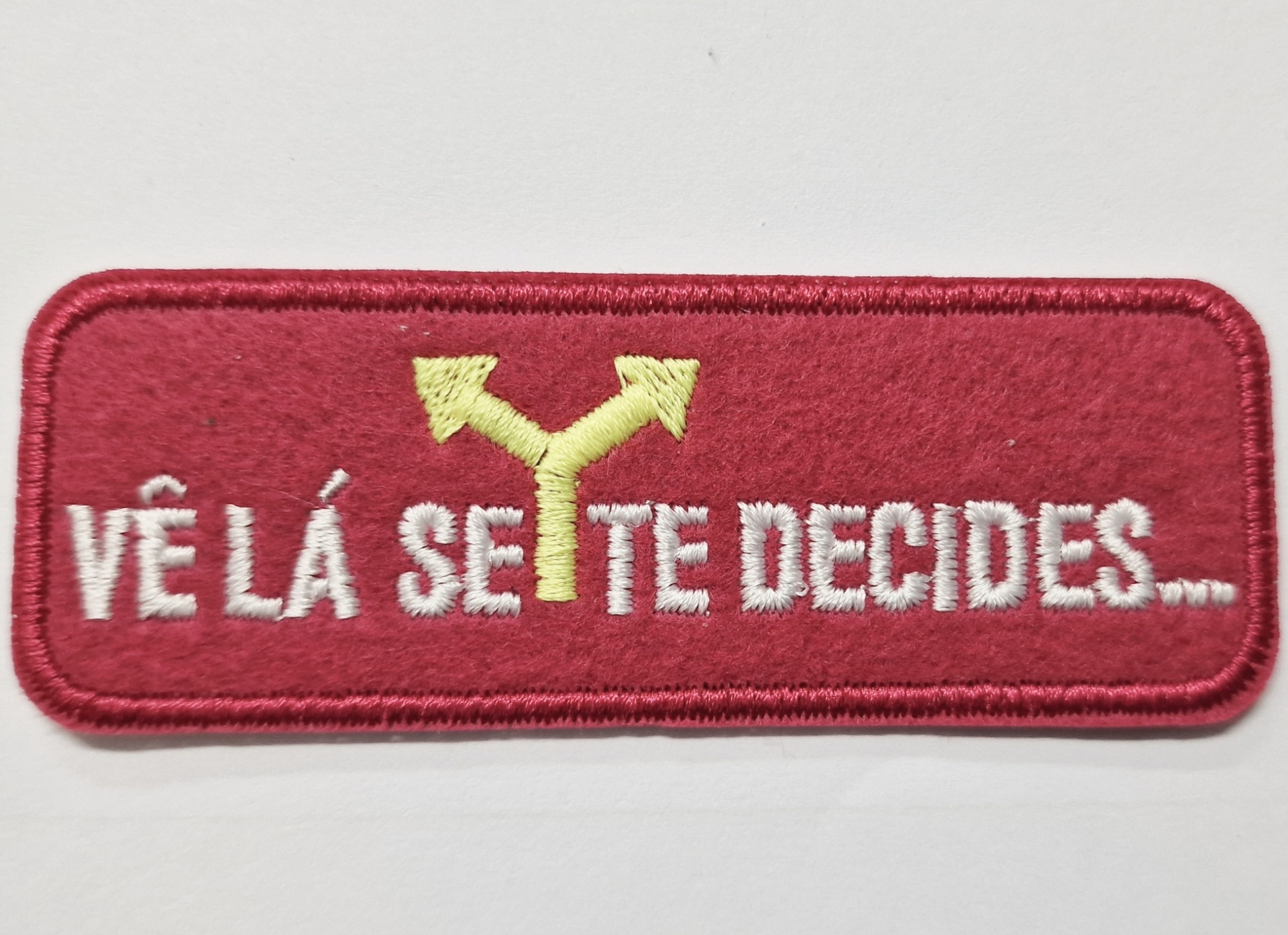 Emblema bordado vermelho com seta amarela e texto branco
