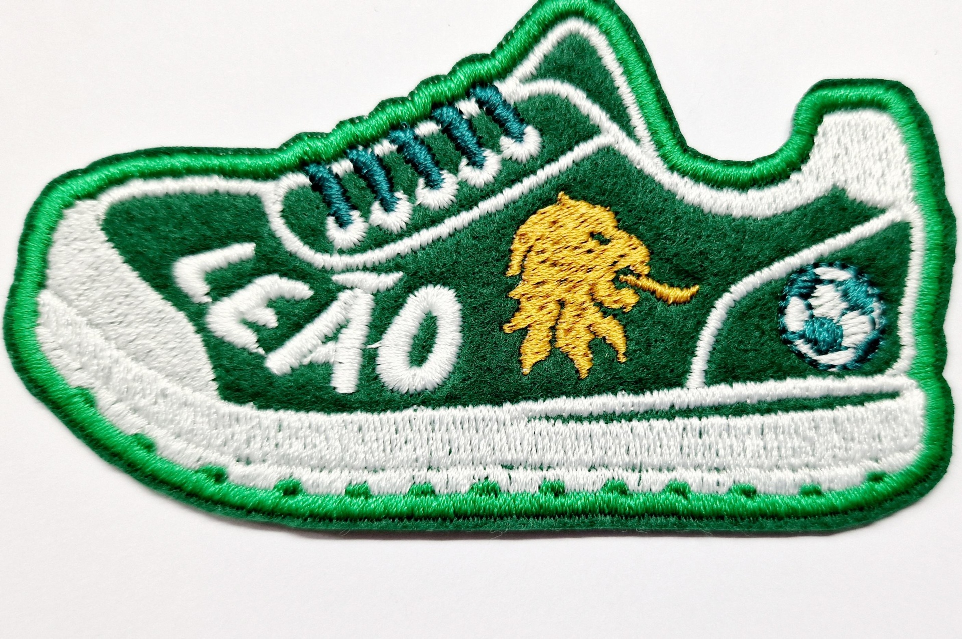 Emblema bordado em forma de sapatilha com texto LEÃO e cabeça de leão