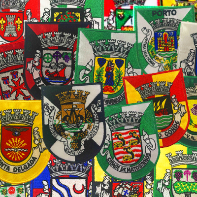 Conjunto de pequenas bandeiras com brasões e nomes de cidades europeias.