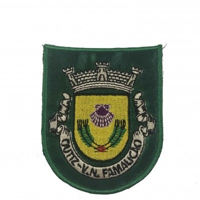 Emblema bordado verde escuro com escudo amarelo, concha roxa, ramos verdes, coroa cinza e texto MUN. DE V.N. FAMALICÃO