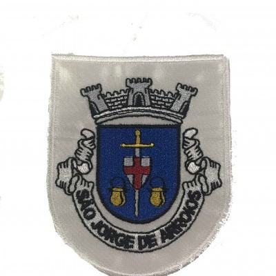 Emblema bordado branco com desenho de castelo, espada e sinos, texto 'SANTO ANTONIO DE MACAO'