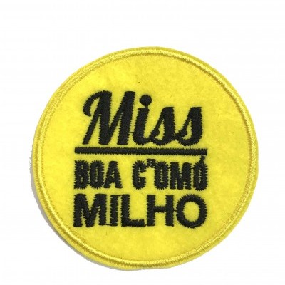 Emblema redondo amarelo com texto bordado preto 'Miss BOA COMÚ MILHO'