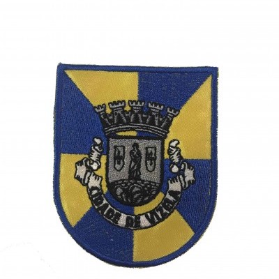 Emblema bordado com escudo azul e amarelo e brasão central cinza.