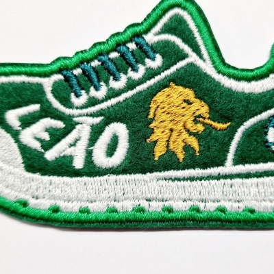 Emblema bordado em forma de sapatilha com texto LEÃO e cabeça de leão