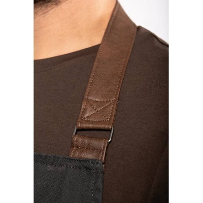Alça de avental castanha em couro sintético sobre t-shirt castanha escura