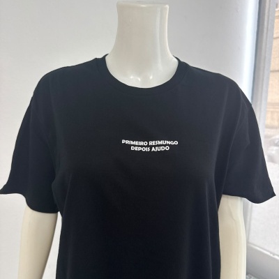 T-shirt preta com texto branco PRIMEIRO RESMUNGO DEPOIS AJUDO exibida em manequim.
