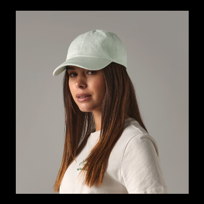 Boné verde claro em tecido com aba curva usado por mulher com camisola branca.