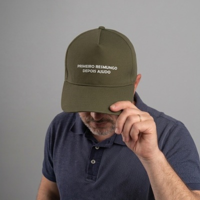Boné verde militar com texto branco usado por homem com camisola azul.