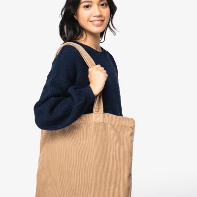 Mala tote de veludo cotelê bege sobre ombro de modelo com camisola azul escuro