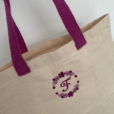 Saco de tecido bege com alças roxas e bordado roxo com letra F