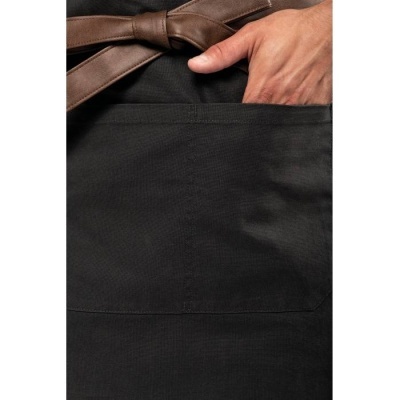 Avental preto com bolso e cinto castanho visto de perto com mão apoiada no bolso
