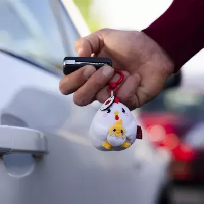 Chaveiro de pelúcia em forma de galinha com pintinhos na mão junto a porta de carro