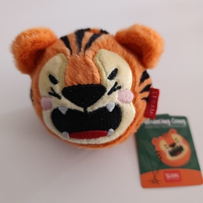 Pelúcia redonda de tigre laranja com olhos e boca bordados, ao lado etiqueta com texto