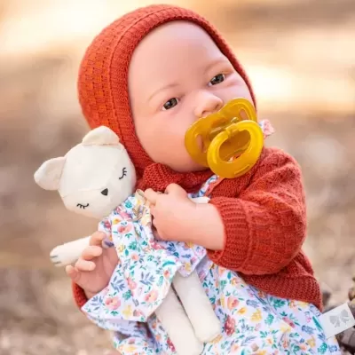 Boneca realista com casaco vermelho e chupeta amarela segurando ursinho de peluche com vestido floral