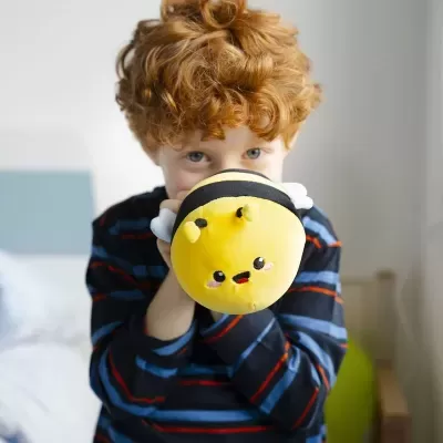 Criança segura peluche amarelo preto em forma de abelha em quarto