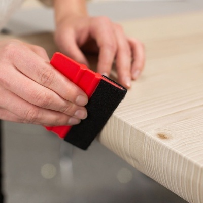 Esponja vermelha e preta a ser usada numa mesa de madeira clara