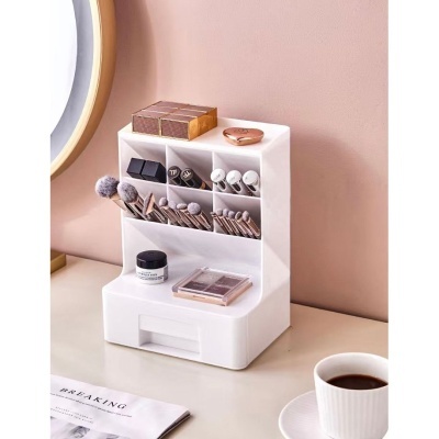 Organizador branco de maquilhagem com pincéis e produtos sobre mesa clara e parede cor de rosa