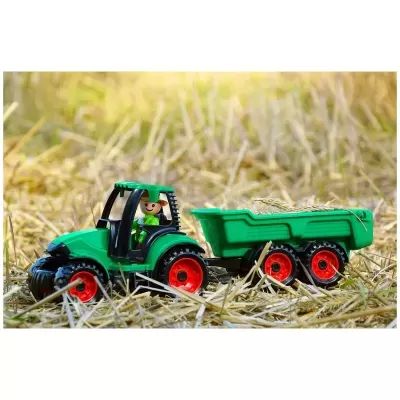 Trator de brinquedo verde com reboque e boneco sobre palha