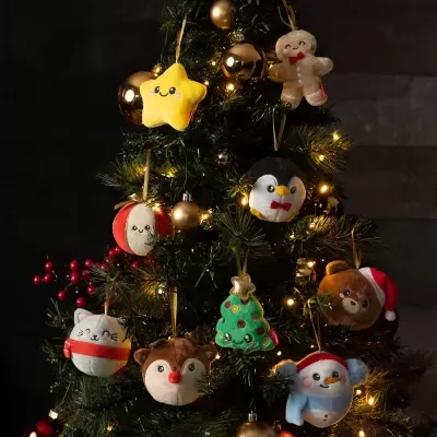 Decorações natalícias de pelúcia em várias formas coloridas penduradas numa árvore de Natal iluminada.