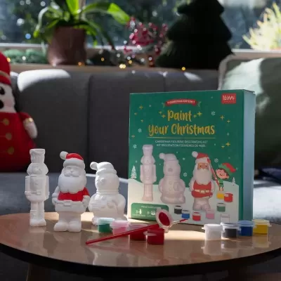 Kit de figuras de gesso para pintura de Natal com tintas coloridas e pincel numa mesa.