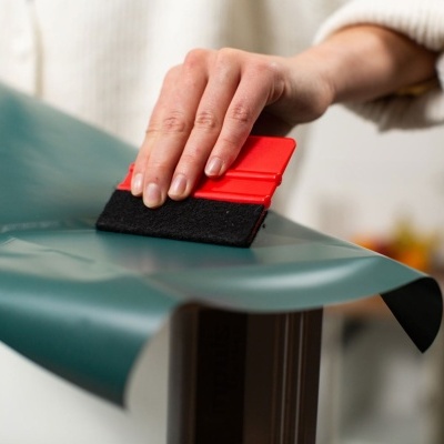 Pessoa usando uma espátula para aplicar vinil verde numa superfície de madeira