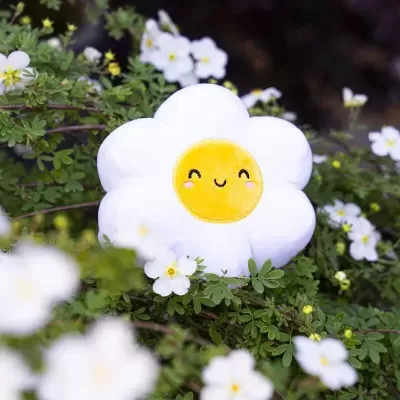 Almofada em forma de flor sorridente entre folhagem e flores brancas