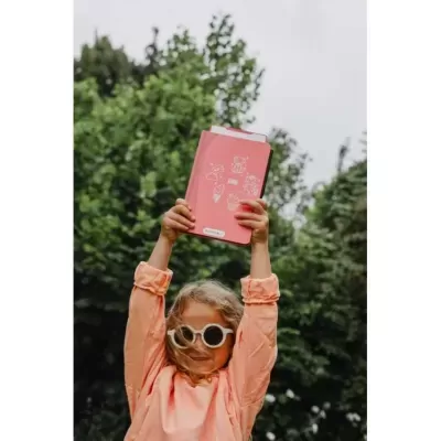 Caderno cor de rosa com desenhos e criança com óculos escuros ao ar livre