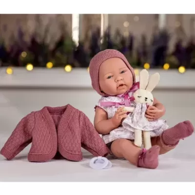 Boneca bebé realista com roupa lilás segurando brinquedo de coelho, casaco de malha e chupeta ao lado