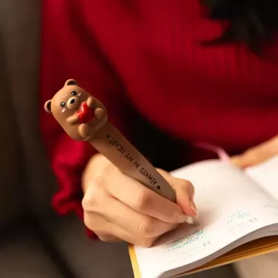 Caneta castanha com ursinho segurando coração vermelho em cima.