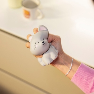 Brinquedo anti-stress cinzento em forma de gato na mão de pessoa com camisola cor-de-rosa