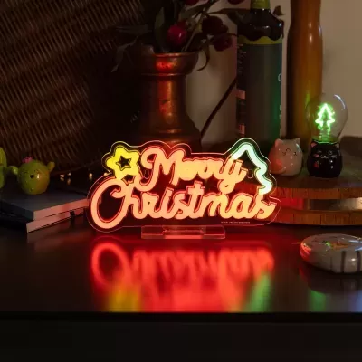 Placa luminosa decorativa com texto Merry Christmas em várias cores numa mesa escura