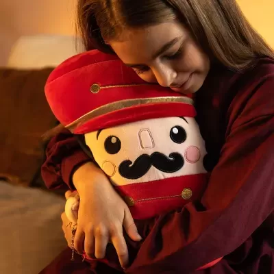 Rapaz abraça almofada de pelúcia de soldado vermelho com bigode e chapéu dourado