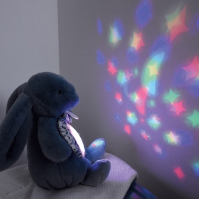 Coelho de peluche azul a projetar luzes coloridas de estrelas na parede