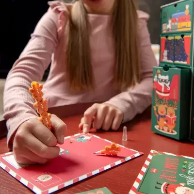 Criança a escrever carta de Natal com caneta decorada, caixas natalícias ao lado