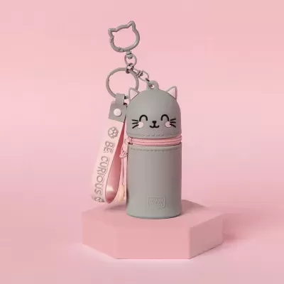 Estojo pequeno cinzento em forma de gato com fecho rosa e chaveiro, sobre suporte rosa