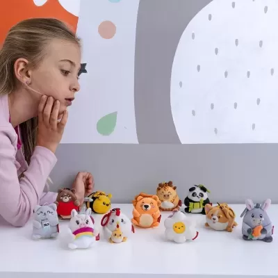 Menina a observar bonecos de pelúcia coloridos de animais pequenos numa mesa branca.