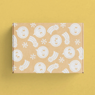 Caixa de cartão castanha com padrão branco de smileys e arcos-íris sobre fundo amarelo.