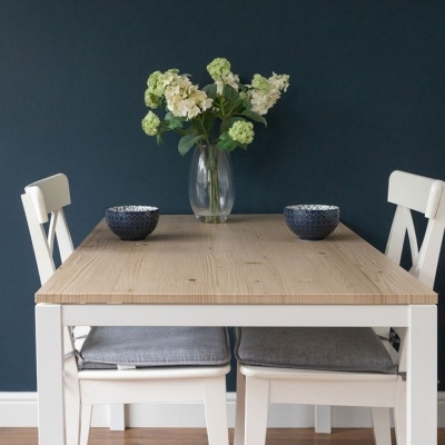 Mesa de madeira clara com cadeiras brancas, recipientes azuis e vaso com flores