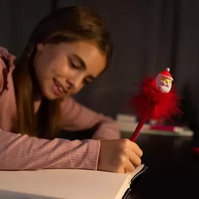Caneta decorativa de Pai Natal com penas vermelhas numa mão de criança escrevendo num caderno