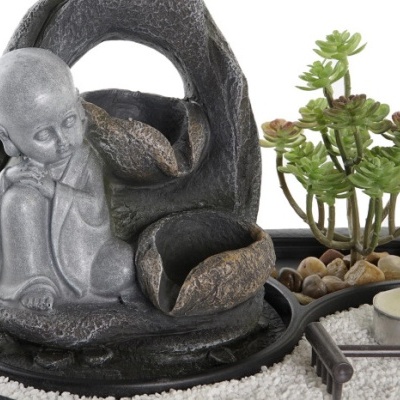 Fonte decorativa com figura de menino meditativo, planta suculenta e areia branca