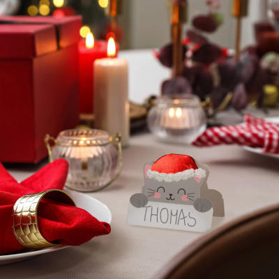 Cartão marcador de lugar gato com gorro de Natal e nome Thomas numa mesa de jantar festiva