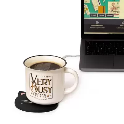 Caneca branca com texto e suporte em forma de gato ao lado de portátil preto
