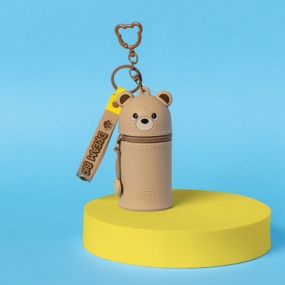 Estojo chaveiro urso bege com etiqueta DREAM BIG sobre suporte amarelo