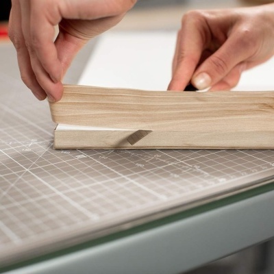 Mãos a segurar fita de madeira clara sobre mesa quadriculada