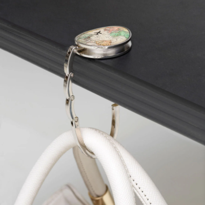 Gancho metálico de mala com decoração floral e pássaro pendurado numa mesa preta