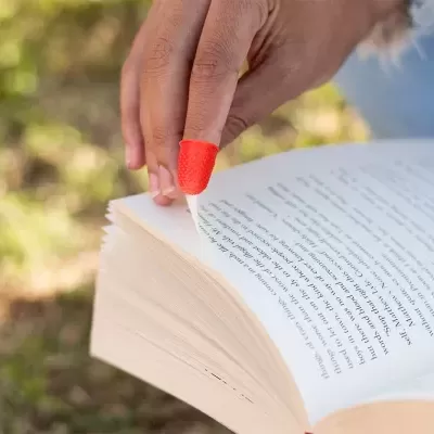 Mão com protetor vermelho de silicone a virar página de livro ao ar livre