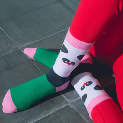 Meias coloridas com padrão de rosto de panda e leggings vermelhas sentada no chão de azulejos