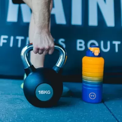 Kettlebell preto 16KG e garrafa desportiva colorida em ambiente de ginásio